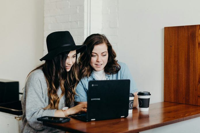 Photo by Brooke Cagle two woman sitting near table using Samsung laptop